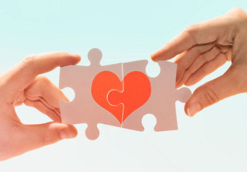 Two hands putting puzzle pieces of a heart together, representing a positive development in marriage counseling near you