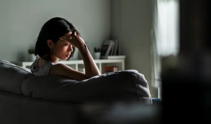 A depressed woman sitting on the couch and holding her head, in need of counseling services in Peoria IL